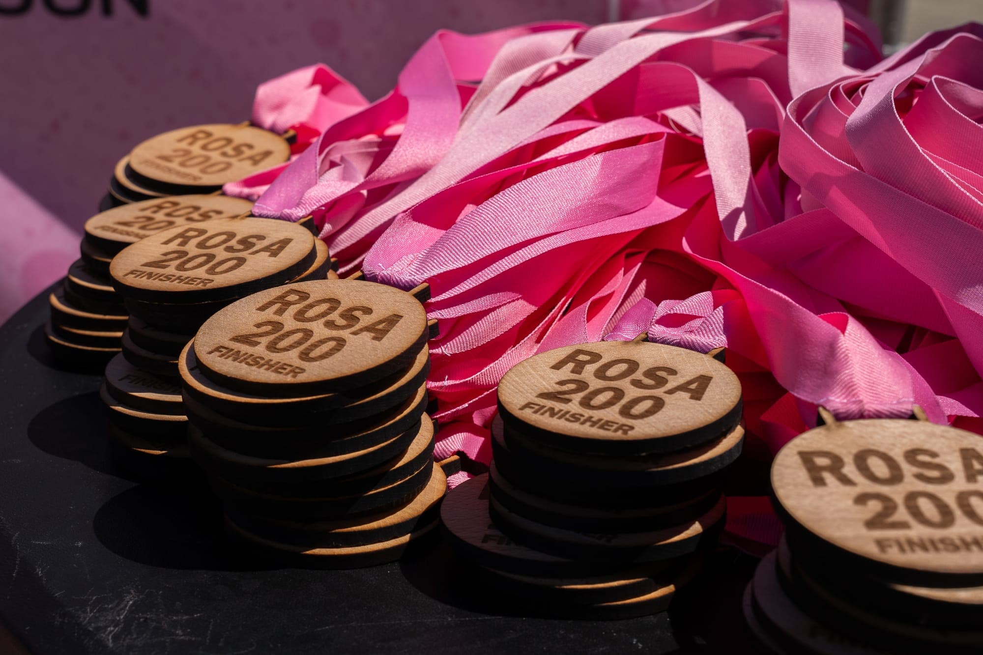 Holzmedaillen mit der Aufschrift Rosa200 Finisher und rosa Bändern