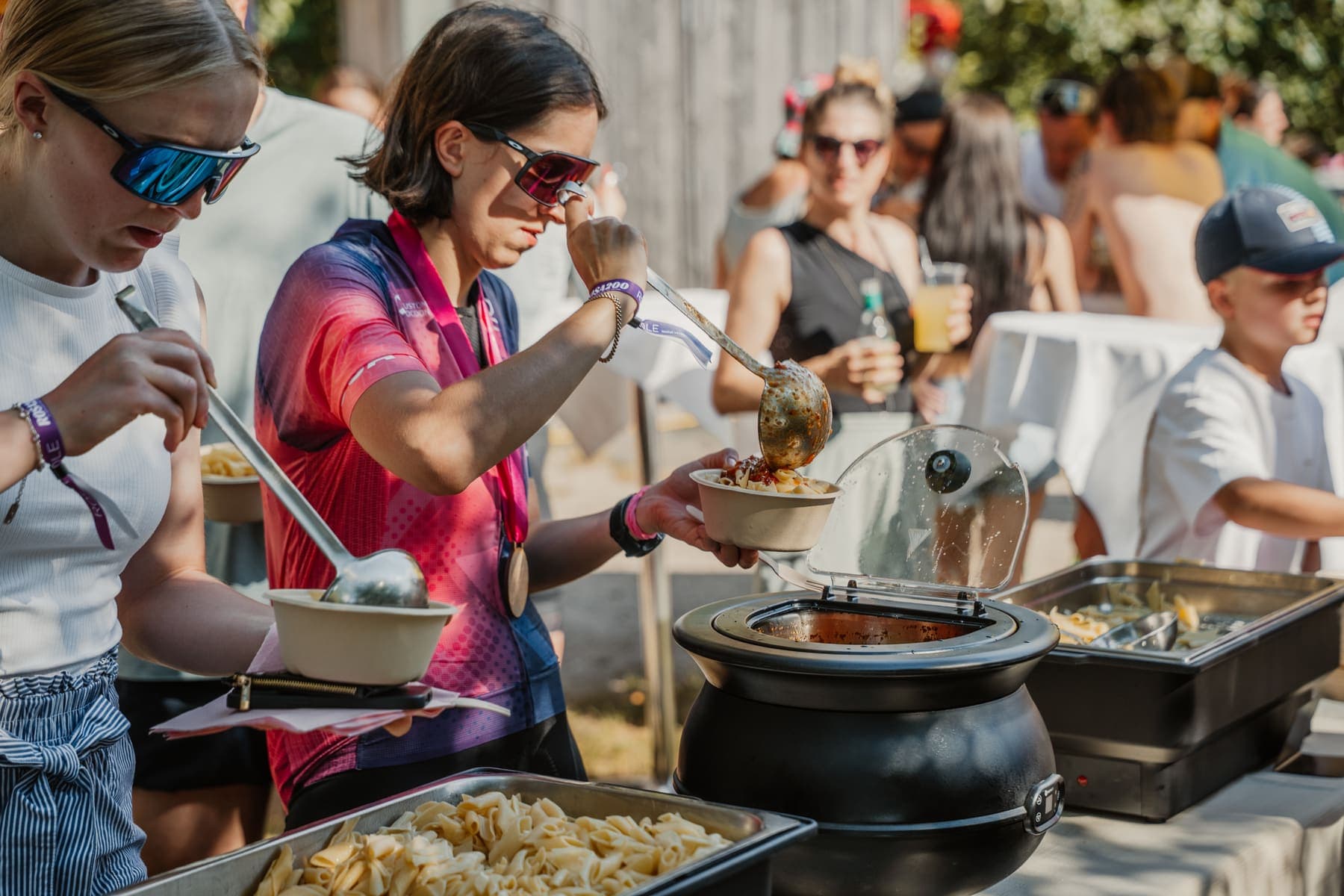 Helferinnen schöpfen Pasta und Sauce in Schüsseln